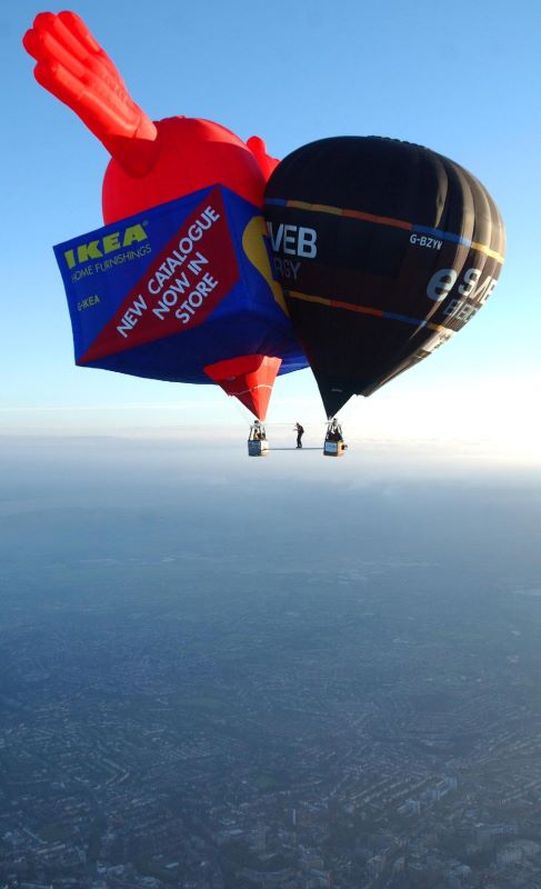 A distance aerial shot of both the box and heart IKEA balloon and round SWEB balloon with Mike walking on the aluminium bar between them.